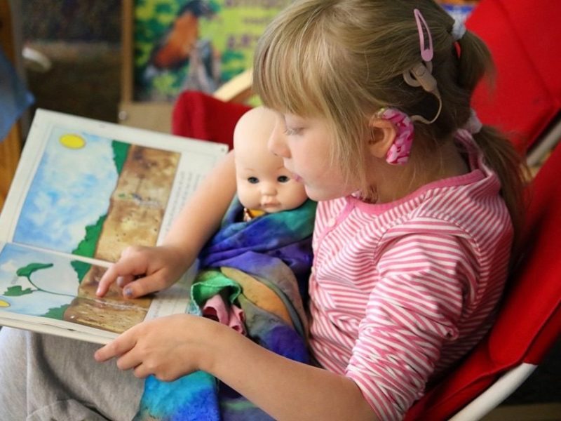 Seven year old girl reading book to doll.