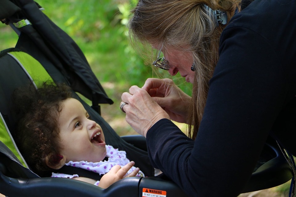 Child in baby carriage looking up and smiling at Mom.