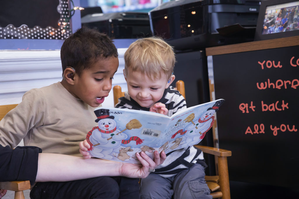 Two five year old boys sitting together reading a book.