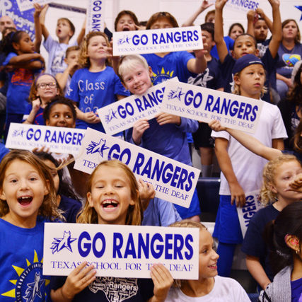 Students wearing blue tee shirts, holding "Go Rangers" signs.