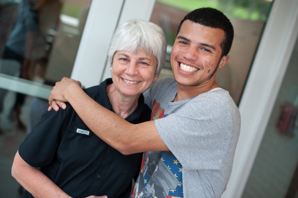 Teenage boy hugging middle aged woman, both smiling.