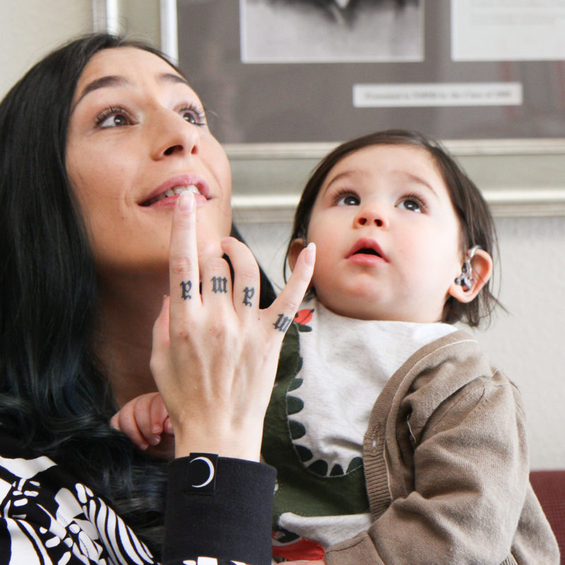Dark haired woman with "Mama" tattooed on hand looking at something above with baby also sharing the view.