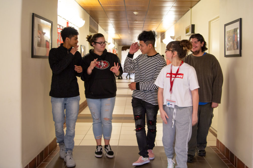 Five high schoolers walking down a school hall.