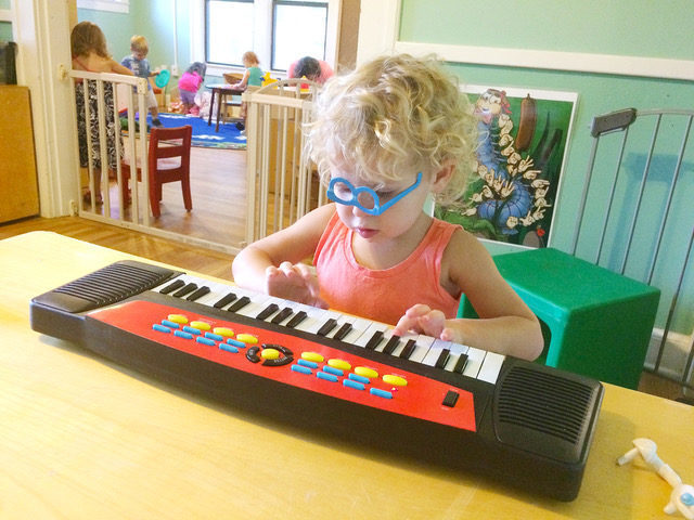 Young blond child with upside down blue glasses playing a desktop organ.