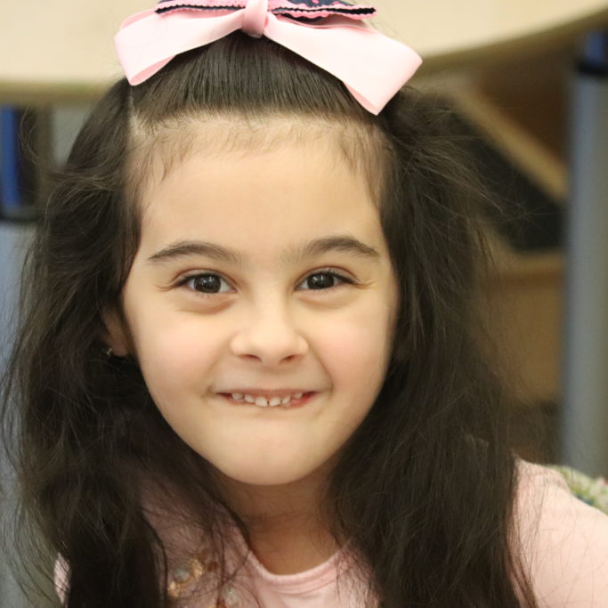 Smiling six year old girl with pink bow in hair.