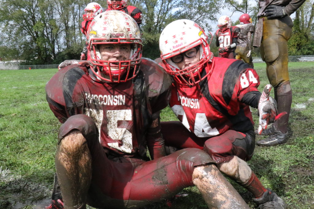 Two muddy football players in red uniforms.