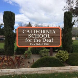 Brown sign with "California School for the Deaf" in white letters, against an outdoor background.