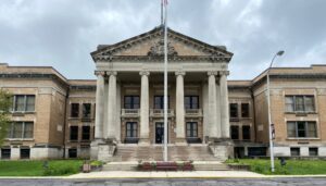 Two story light brick building with columns in front.